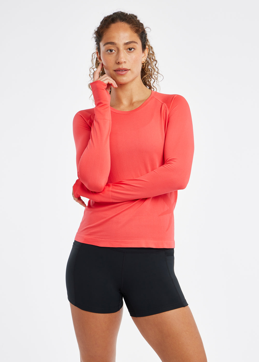 Woman wearing a red orange running long sleeve and black compression shorts, front view