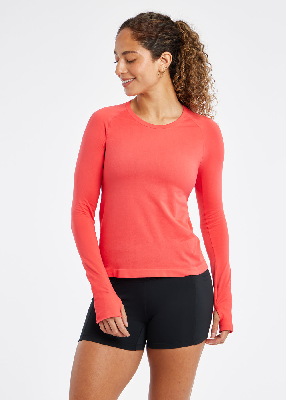 Woman wearing a red orange running long sleeve and black compression shorts, alternate front view